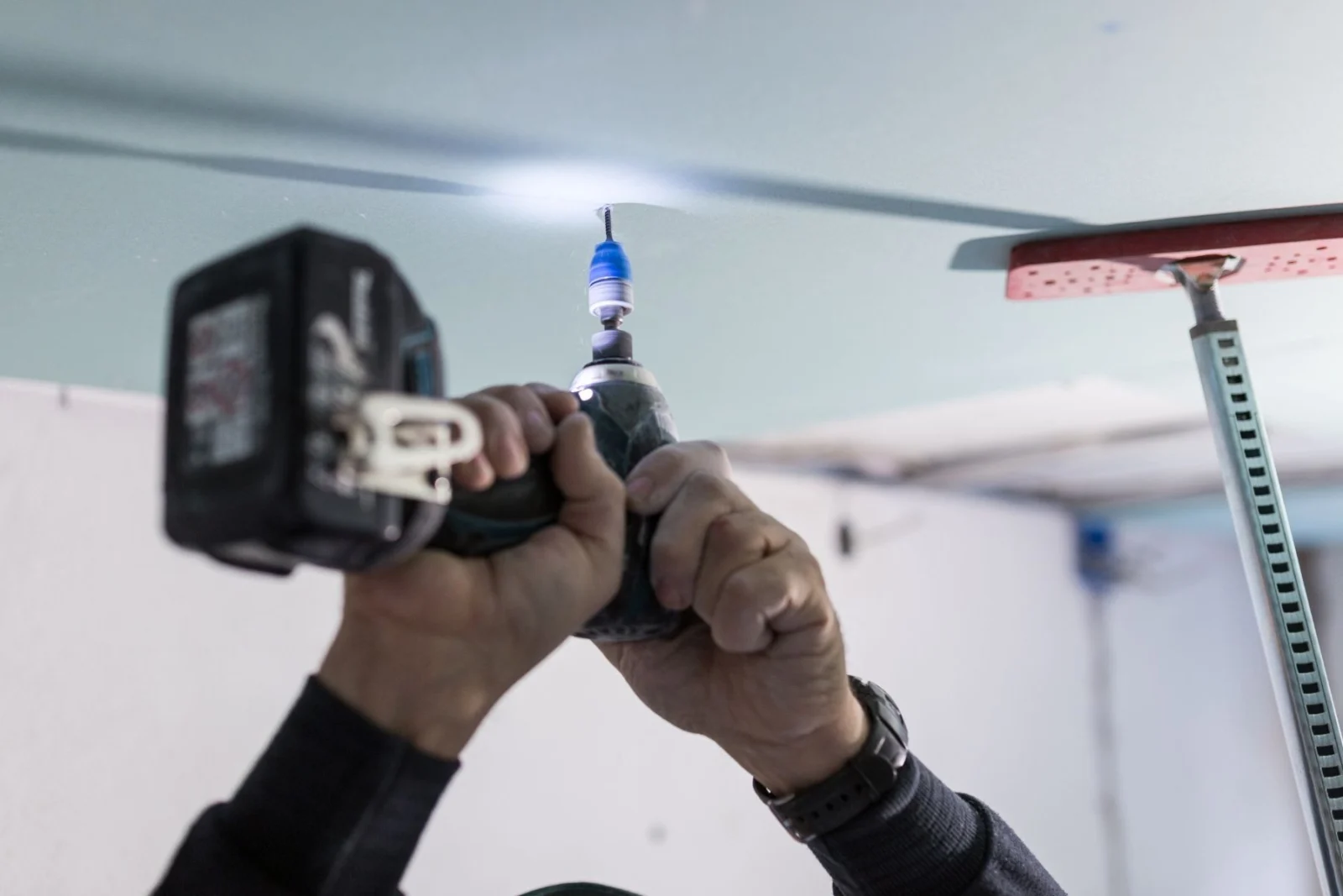 Plasterer using a drill to fix ceiling sheets